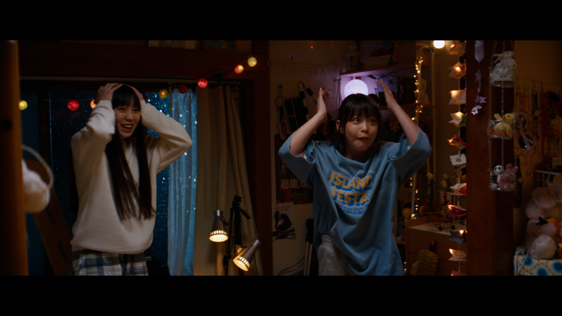 映画の場面。二人の娘が楽しそうに手を頭に添えている